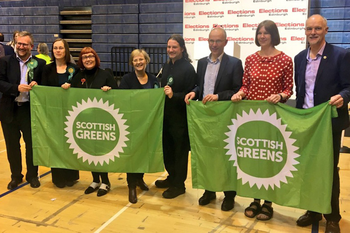 8 Green winning councillors at the Edinburgh count, holding Scottish Green flags