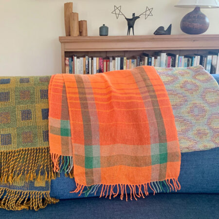 Three woven scarves in different designs on the back of a sofa